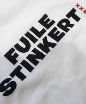Print met de tekst fuile stinkert in zwart op wit t-shirt met kleine rode Andreaskruizen ernaast.